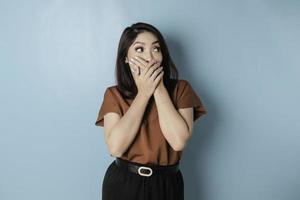 un portrait d'une femme asiatique choquée portant une chemise marron, isolée par un fond bleu photo