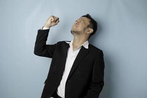 un jeune homme asiatique avec une expression heureuse et réussie portant un costume isolé sur fond bleu photo