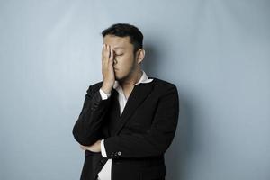 l'homme d'affaires asiatique a l'air fatigué et déprimé, a une expression triste tout en se tenant la tête. fond bleu isolé photo