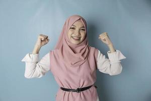 femme musulmane asiatique excitée portant un hijab rose montrant un geste fort en levant les bras et les muscles en souriant fièrement photo