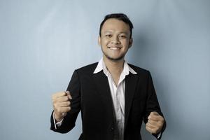 un jeune homme asiatique avec une expression heureuse et réussie portant un costume isolé sur fond bleu photo