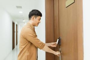 main d'homme asiatique tenant une carte d'accès, porte électronique à carte-clé scannant le contrôle d'accès pour verrouiller et déverrouiller la porte photo