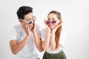 concept de geste et de personnes - portrait d'un couple heureux en lunettes de soleil et t-shirts blancs, touche les joues avec les deux mains sur fond blanc photo