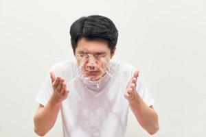 jeune homme pulvérisant de l'eau sur son visage sur fond blanc photo