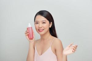 portrait d'une jeune femme tenant des bouteilles roses avec de la lotion sur fond blanc photo