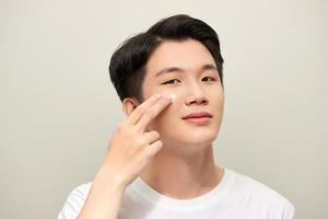 portrait en gros plan d'un jeune homme asiatique souriant et heureux avec une crème hydratante appliquée sur le visage. photo