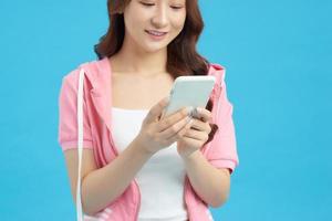 souriante belle jeune femme debout et utilisant un téléphone portable sur fond bleu photo