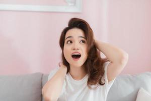 jeune femme asiatique levant les mains à la tête, la bouche ouverte, se sentant extrêmement chanceuse, surprise, excitée et heureuse contre le mur rose photo