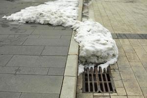 la neige fond à la grille d'égout. élimination de l'eau de fonte de la rue. photo