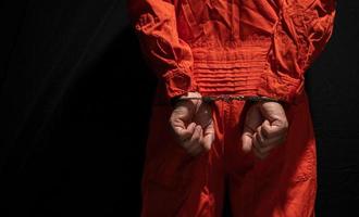 menottes sur un criminel accusé en combinaison de prison orange. délinquant condamné à purger une peine de prison, sur fond noir photo