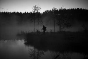 homme dans le brouillard sur le lac. l'homme marche vers l'eau. brouillard mystique dans la forêt. loisirs de plein air. photo