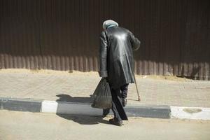 une vieille femme avec un bâton de marche descend la route. retraité en russie. manteau noir. photo