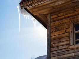 Glaçon illuminé par le soleil sur le toit de la vieille maison en rondins photo