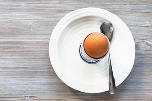 Oeuf brun dans une tasse et une cuillère sur une plaque blanche sur gris photo