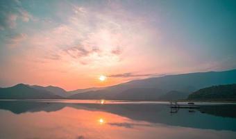 panorama panoramique du lac de montagne avec une réflexion parfaite au lever du soleil. beau paysage de chaîne de montagnes avec un ciel pastel rose avec des collines sur fond et reflété dans l'eau. paysage de lac nature