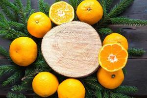 fond de vacances du nouvel an sur une coupe ronde d'arbre entouré de mandarines, de branches de sapin vivantes et de guirlandes de lumières dorées, avec un espace en bois pour le texte. arôme d'agrumes, tranches d'orange, noël. Cadre photo