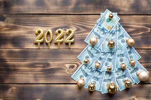 sapin de noël composé de billets de 100 dollars sur fond de bois avec fond et 2022. décor de noël de la finance, de l'épargne, de la richesse, des dépenses du nouvel an. catégoriquement. pile de 100, investissements, affaires photo