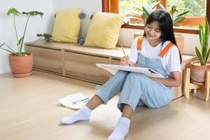 jeune fille assise sur le sol et peignant sur papier à la maison. passe-temps et étude d'art à la maison. photo