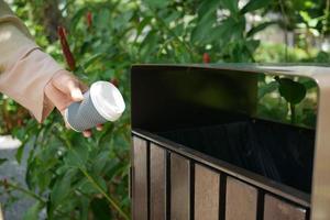 main de femme jetant une tasse de café en papier vide dans la poubelle ou la poubelle photo