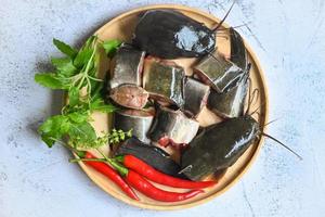 poisson-chat pour la cuisson des aliments, poisson haché avec des ingrédients herbes et épices, menu de poisson-chat cru frais poisson d'eau douce, filet de poisson-chat sur une assiette en bois photo