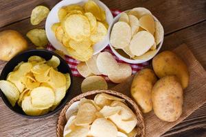 collation de croustilles sur bol et assiette, croustilles croustillantes sur la table de la cuisine et pommes de terre crues fraîches sur fond de bois photo