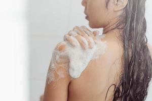 jeune femme lavant le corps sous la douche. une femme asiatique prend un bain dans la salle de bain. photo