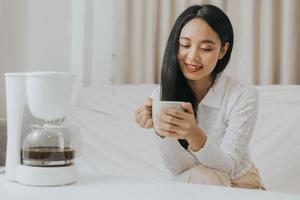 femme heureuse souriant et faisant du café à la maison. femme asiatique appréciant et sentant le café chaud le matin. photo