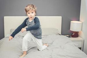 petit garçon en pyjama jouant sur le lit. photo