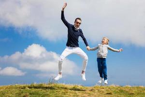 joyeux père et fils se tenant la main et sautant contre le ciel. photo