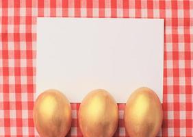 oeufs de pâques dorés sur fond de nappe à carreaux rouges avec carte de voeux blang, joyeuses fêtes de pâques photo