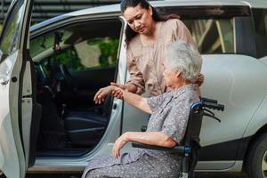 le soignant aide une patiente asiatique âgée handicapée à monter dans sa voiture, concept médical. photo