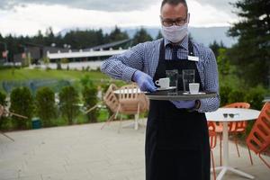 un serveur portant un masque de protection médicale sert le café au restaurant photo