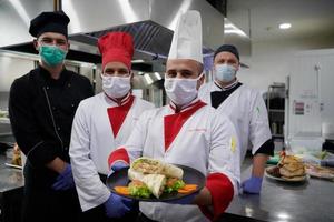 chefs de groupe debout ensemble dans la cuisine du restaurant portant un masque médical de protection et des gants dans le nouveau concept normal de coronavirus photo