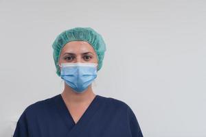 gros plan d'une femme médecin ou scientifique avec un masque médical et une casquette chirurgicale sur fond gris. elle ajuste le masque avec photo