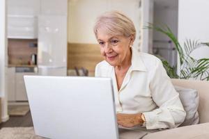 dame âgée travaillant avec un ordinateur portable. portrait d'une belle femme plus âgée travaillant à l'intérieur d'un ordinateur portable. femme âgée utilisant un ordinateur portable à la maison, riant photo