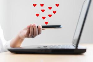 des icônes en forme de coeur apparaissent sur l'écran du téléphone portable pendant qu'une femme travaille sur un ordinateur portable. photo