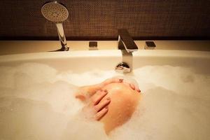 dame dans la baignoire avec une bulle pleine nettoyant sa jambe dans une humeur sexy. photo