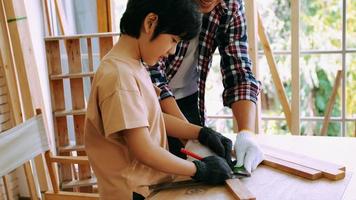 jeune charpentier masculin enseignant à son fils comment travailler le bois en atelier. photo