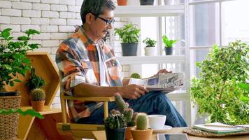 un vieil homme assis dans un salon décoré de pots de fleurs. photo