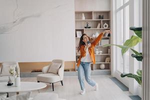 femme hispanique heureuse chantant à la maison avec un téléphone portable comme avec un microphone. écoute de musique en ligne. photo