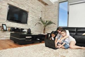 une jeune famille heureuse s'amuse et travaille sur un ordinateur portable à la maison photo