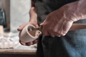 mains découpant une tasse en bois, travaillant avec un ciseau en gros plan. atelier en bois. processus de fabrication d'ustensiles de cuisine en bois photo