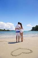 couple romantique amoureux s'amuser sur la plage avec coeur s'appuyant sur le sable photo