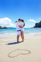 couple romantique amoureux s'amuser sur la plage avec coeur s'appuyant sur le sable photo