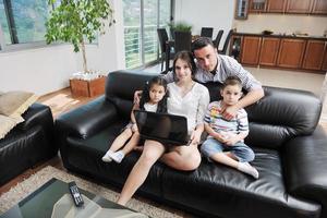 une jeune famille heureuse s'amuse et travaille sur un ordinateur portable à la maison photo