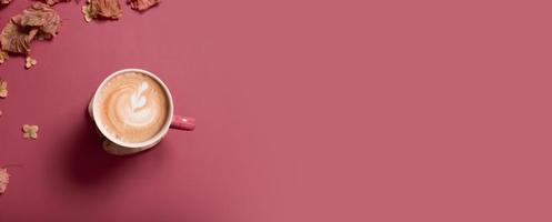 bannière plate d'automne avec des feuilles sèches et une tasse de café au lait sur fond de couleur rose foncé. automne créatif, action de grâces, automne, concept d'halloween. vue de dessus, espace de copie photo