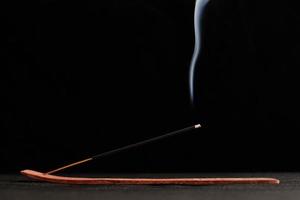 boucles de fumée de bâton d'encens brûlant dans un support en bois pour la relaxation et la méditation fond noir photo