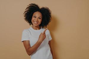 jeune modèle féminin africain positif en chemise blanche indiquant avec l'index à l'espace de copie vierge photo