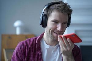 jeune homme allemand souriant dans les écouteurs à l'aide de l'application de traduction sur téléphone mobile tout en étudiant en ligne photo