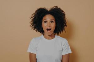 étonné stupéfait femme à la peau sombre regardant la caméra avec la bouche ouverte isolée sur un mur beige photo